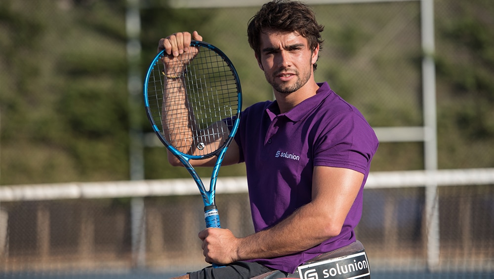 Daniel Caverzaschi con polo de Solunion y una raqueta en la pista de tenis